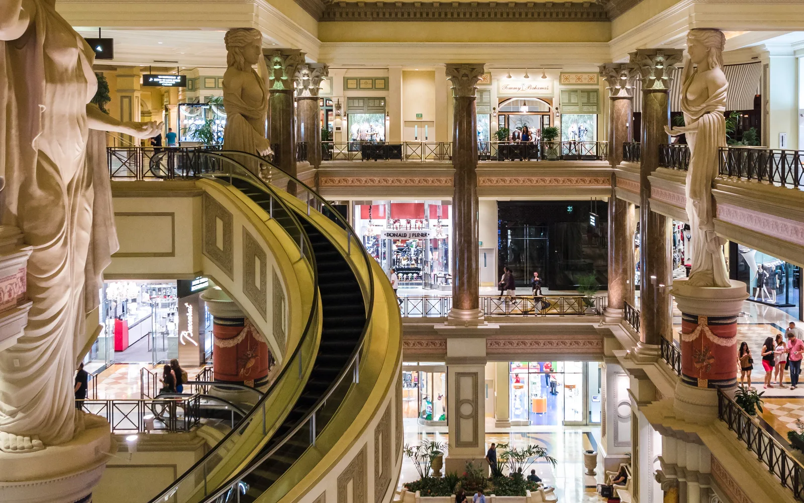 A modern shopping center interior with retail storefronts, skylighting, and architectural details